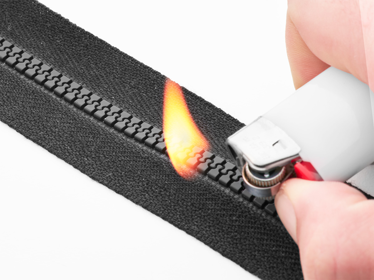 Black zipper with lighter flame demonstrating fire resistance